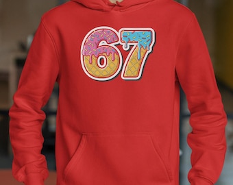 May include: A red hooded sweatshirt featuring a large, colorful graphic of the number "67." The "6" is designed as a donut with pink frosting and sprinkles, while the "7" resembles an ice cream cone with blue frosting.