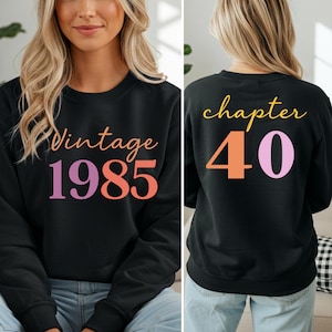 Può includere: Felpa nera con la scritta "Vintage 1985" in arancione e viola sul davanti. Il retro della felpa dice "chapter 40" in giallo, arancione e viola. Girocollo.