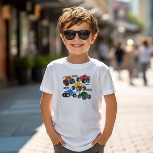 Puede incluir: Camiseta blanca con un dise&ntilde;o de seis monster trucks de colores. Los camiones son naranja, rojo, amarillo, azul y verde, con ruedas grandes. La camiseta es de manga corta y parece ser de algod&oacute;n.
