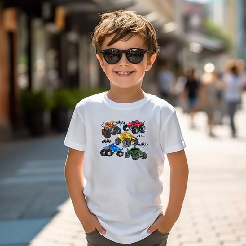 Puede incluir: Camiseta blanca con un dise&ntilde;o de seis monster trucks de colores. Los camiones son naranja, rojo, amarillo, azul y verde, con ruedas grandes. La camiseta es de manga corta y parece ser de algod&oacute;n.