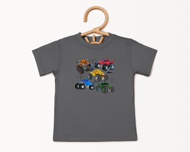 Puede incluir: Una camiseta gris carb&oacute;n con un gr&aacute;fico colorido de cinco monster trucks. Los camiones son de varios colores, incluyendo naranja, rojo, amarillo, azul y verde, con dise&ntilde;os detallados y banderas a cuadros.