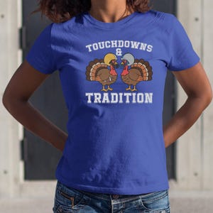 May include: Royal blue t-shirt with the words "Touchdowns & Tradition" in white block letters. Two cartoon turkeys wearing football helmets are featured in the center. The turkeys are brown with red wattles and tail feathers.