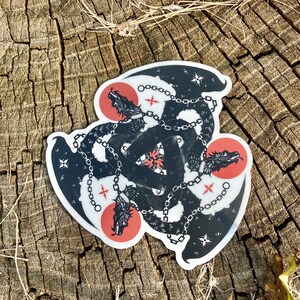 May include: Black and white sticker of three dragons chained together in a triangular formation. The dragons are facing outward with their mouths open. The background is red and white.