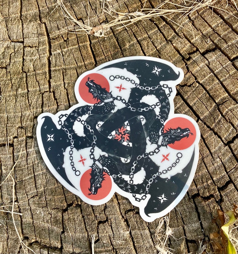 May include: Black and white sticker of three dragons chained together in a triangular formation. The dragons are facing outward with their mouths open. The background is red and white.