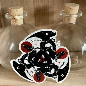 May include: Black and white sticker of three chained dragons forming a triangle with red circles behind each dragon head.