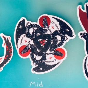 May include: Three black and red dragon stickers with different designs. The left sticker shows a dragon curled around a red circle. The middle sticker shows three dragons intertwined with chains. The right sticker shows a dragon with its wings spread out.