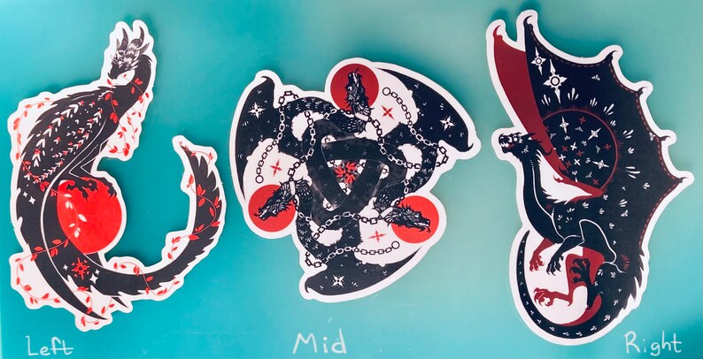 May include: Three black and red dragon stickers with different designs. The left sticker shows a dragon curled around a red circle. The middle sticker shows three dragons intertwined with chains. The right sticker shows a dragon with its wings spread out.