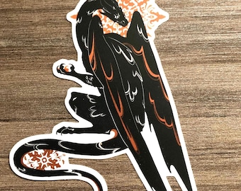 May include: Black and orange silhouette of a dragon with wings spread wide. The dragon is curled around a circular design with intricate details.