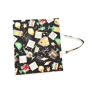 May include: A black fabric tote bag with a colorful dessert-themed pattern. The pattern includes images of ice cream, gingerbread houses, and candy. The bag has a matching strap and silver-colored metal hardware.
