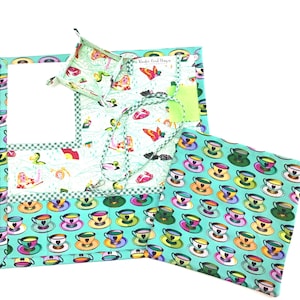 May include: A teal fabric organizer with a white background and a variety of colorful patterns. The organizer has a pocket for a notepad and a small box for holding items. The organizer is made of fabric and has a teal and white checkered border.