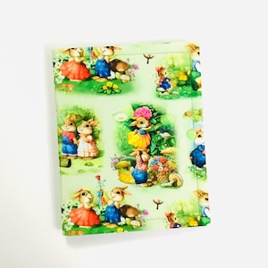 May include: A green fabric with a repeating pattern of bunnies in various poses. The bunnies are wearing colorful clothing and are surrounded by flowers and greenery.