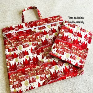 May include: A red and white fabric bag and matching square pouch. The fabric features a repeating pattern of red houses, trees, and gold accents on a white background. The bag has a zipper closure and a handle. Text on the image reads: Floss bed folder. Sold separately.