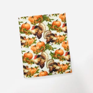May include: A rectangular fabric item with a repeating pattern of pumpkins and turkeys. The pumpkins are orange, and the turkeys are brown with red and white accents. Green leaves and vines are also present.