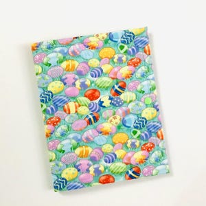 May include: A green fabric with a pattern of colorful Easter eggs. The eggs are various shapes and sizes and have different patterns.