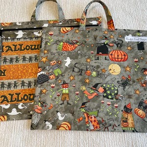 May include: Two square fabric tote bags featuring a Halloween theme. The front bag displays witches, pumpkins, black cats, ghosts, and the word Spooky on a gray background. The back bag shows orange stripes with black cats and the word Halloween.