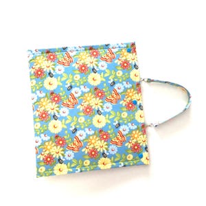 May include: A light blue tote bag with a floral print featuring butterflies, bees, and flowers. The bag has a single strap and is made of fabric.