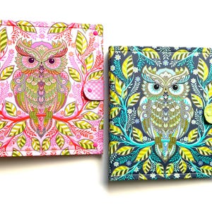 May include: Two fabric-covered journals with owl designs. One journal is pink with a pink and white checkered closure, and the other is blue with a yellow closure. Both feature colorful owl illustrations surrounded by floral patterns.