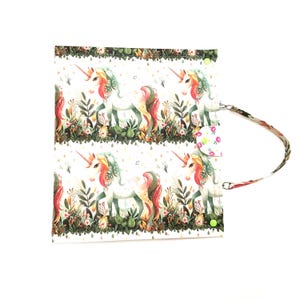 May include: A white, rectangular bag featuring a repeating pattern of colorful unicorns in a whimsical garden setting. The bag has a floral-patterned strap and a button closure. The unicorns have rainbow manes and tails.