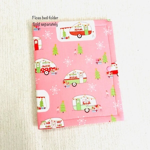 May include: Pink fabric floss bed folder with a repeating pattern of Christmas camper trailers, Christmas trees, snowflakes, and Santa Claus. The folder has a stitched border and the text "Floss bed folder" and "Sold separately".