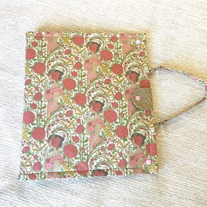 May include: A rectangular fabric portfolio case featuring a repeating pattern of women in pink dresses surrounded by red roses and green foliage. The case includes a gold glitter flap closure with a pink snap button and a matching fabric handle.