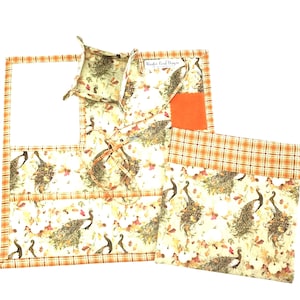 May include: Set of three fabric placemats with a peacock and leaf design. The placemats have a brown and orange plaid border. The placemats are made by "Nooky Bird Designs".