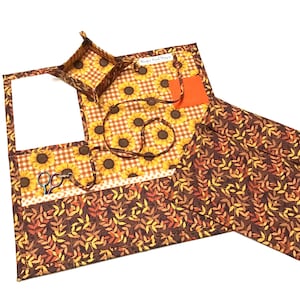 May include: A sewing organizer set with a sunflower and fall leaf pattern. The set includes a tray, a mat with a pocket for scissors, and a matching pouch. The colors are orange, yellow, brown, and white.
