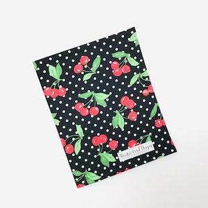 May include: Black fabric with white polka dots and a repeating pattern of red cherries with green leaves. The fabric has a white label with the text "Kreativ Card Design".