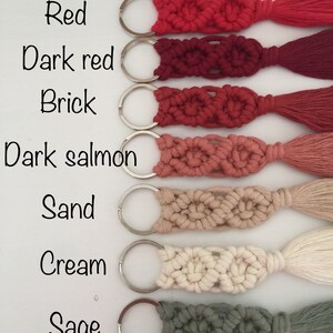 May include: Seven keychains with different colored tassels. The keychains are made of macrame and have a silver key ring. The colors of the tassels are red, dark red, brick, dark salmon, sand, cream, and sage.