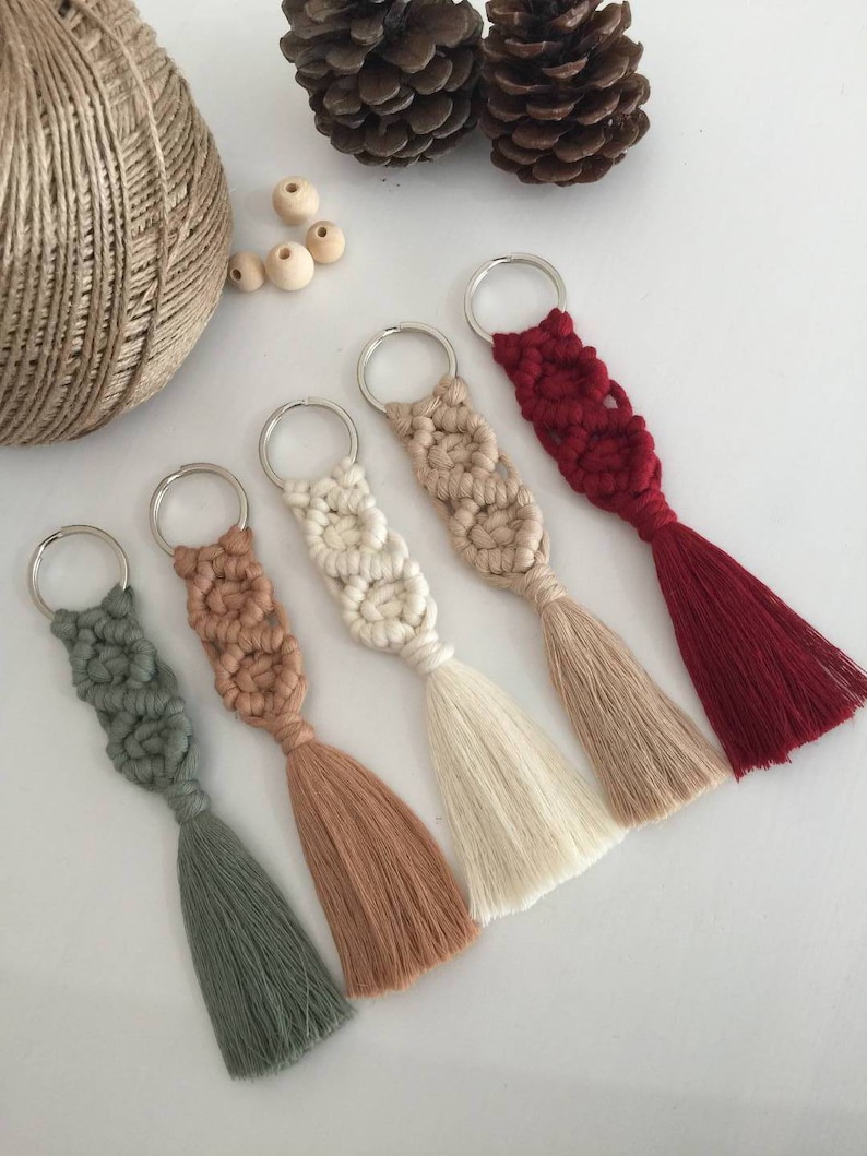May include: Five keychains with tassels in various colors including green, brown, white, beige, and red. The keychains are made of macrame string and have a silver metal ring.