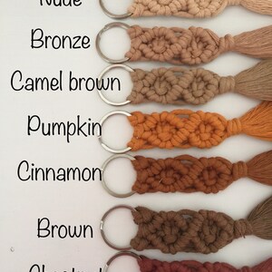May include: Seven keychains with tassels in different shades of brown, from light to dark. The colors are: Nude, Bronze, Camel Brown, Pumpkin, Cinnamon, Brown, and Chestnut. Each keychain has a silver key ring.