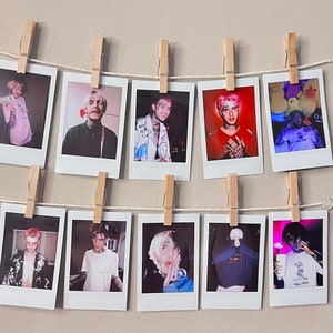 May include: A wall display of 10 Polaroid photos featuring a person with pink hair and various outfits. The photos are hung on a string with clothespins.