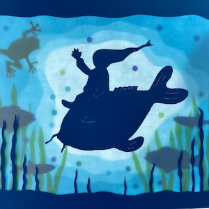 May include: An illustration shows a dark silhouette of a person riding a fish, set against a blue and green underwater backdrop. The scene includes a frog, fish, and aquatic plants, evoking a fantastical underwater environment.