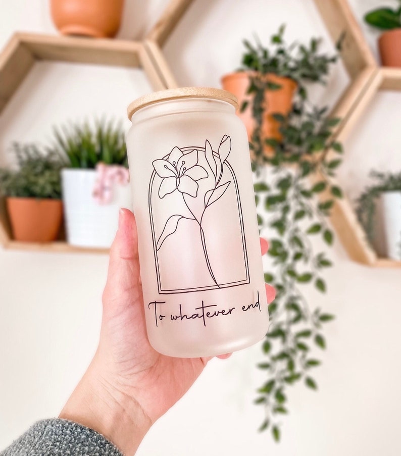 May include: A frosted glass jar with a wooden lid and a black line drawing of a flower. The jar has the text "To whatever end" printed on the front.