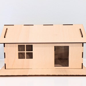 May include: A wooden model of a house with a brown roof, a window, and a door. The house is sitting on a wooden base.