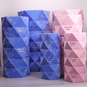 May include: Geometric-shaped boxes in shades of blue and pink are stacked in a display. The boxes have a faceted design and a soft, velvety texture. Each box has the text "Radoylady Flowers" in a cursive font.