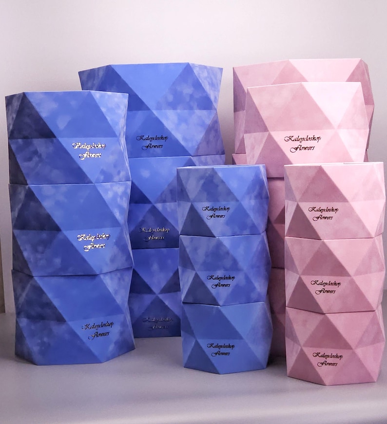 May include: Geometric-shaped boxes in shades of blue and pink are stacked in a display. The boxes have a faceted design and a soft, velvety texture. Each box has the text "Radoylady Flowers" in a cursive font.