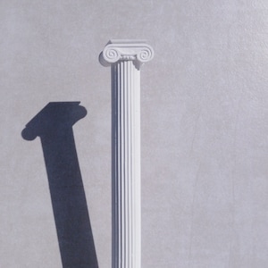 Puede incluir: Columna de yeso blanco con un fuste estriado y una base simple. La columna está sobre una superficie gris.