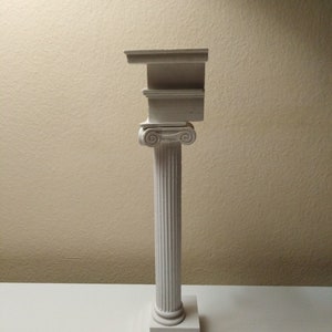 May include: A white plaster model of a column with a base and a capital. The capital is broken and sits on top of the column.