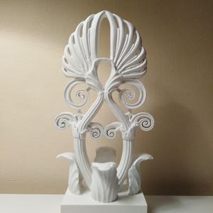 Op de afbeelding: Witte keramische sculptuur van een gestileerde plant met ingewikkelde details. De sculptuur staat op een witte basis.