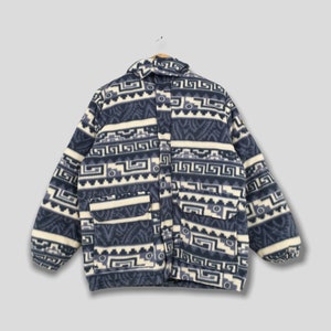 May include: A blue and cream-colored fleece jacket with a geometric pattern. The jacket has a collared neckline, two front pockets, and a button-up closure. The jacket is hanging on a wooden hanger.