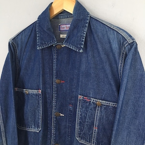 May include: A blue denim jacket with red stitching and brass buttons. The jacket has two chest pockets and two front pockets. The label on the jacket reads "Free Blue".