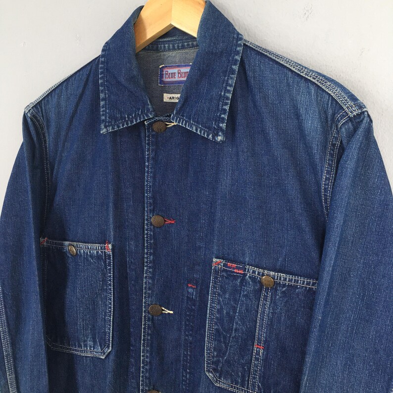 May include: A blue denim jacket with red stitching and brass buttons. The jacket has two chest pockets and two front pockets. The label on the jacket reads "Free Blue".