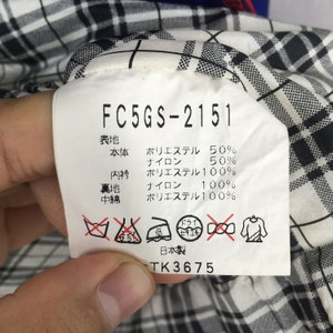 May include: A white tag with black text and symbols, attached to a garment with a black and white plaid pattern. The tag includes the text "FC5GS-2151" and Japanese characters. The tag also lists fabric composition percentages.