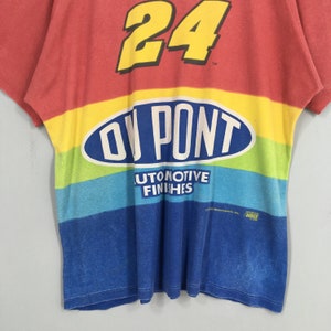 Op de afbeelding: Een vintage t-shirt in rood, geel, blauw en groen, met het nummer 24 in geel. Het shirt toont het DuPont-logo en de woorden "AUTOMOTIVE FINISHES".