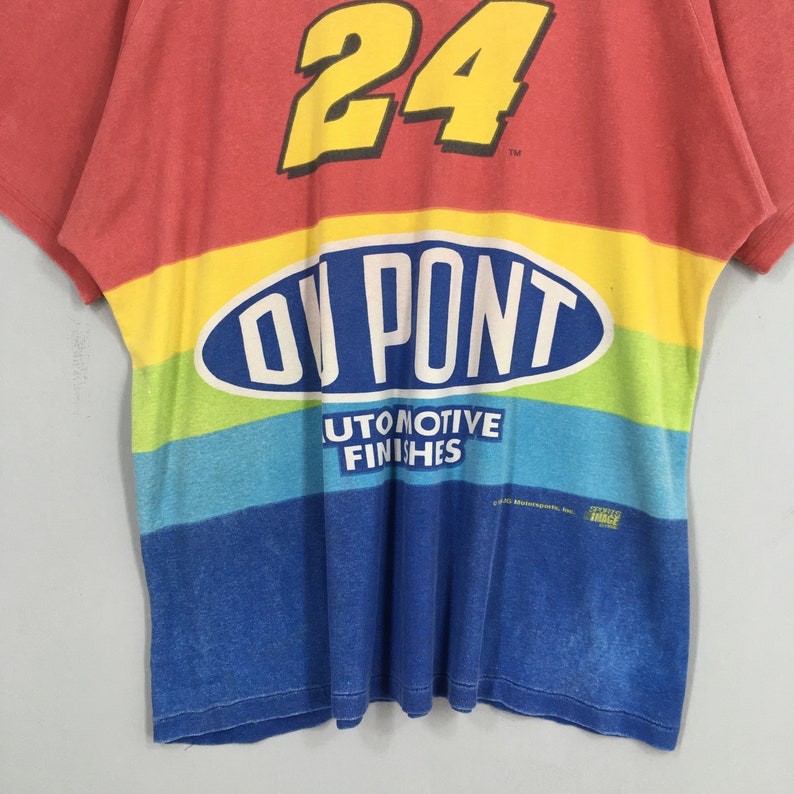 Op de afbeelding: Een vintage t-shirt in rood, geel, blauw en groen, met het nummer 24 in geel. Het shirt toont het DuPont-logo en de woorden "AUTOMOTIVE FINISHES".