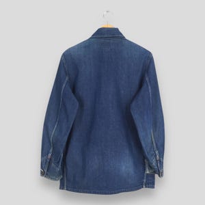 May include: A blue denim work shirt with long sleeves and a button-up front. The shirt is hanging on a wooden hanger.