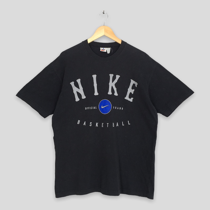 Może przedstawiać: Czarny T-shirt z białym logo Nike i tekstem "NIKE OFFICIAL BRAND BASKETBALL" w stylu vintage.