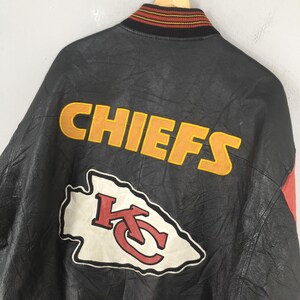May include: Black leather jacket with the word "CHIEFS" in yellow block letters. Below the word is a white and red logo. The jacket has a red accent on the side and a striped collar.