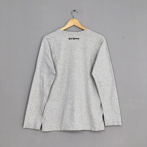 May include: Gray long-sleeve t-shirt with a black print of the artist's signature, "&copy; K. Haring", on the back.