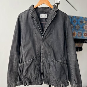May include: A charcoal gray jacket with a notched lapel, two front buttons, and two large patch pockets. The interior label reads Spellbound Genuine Garment. The jacket features visible stitching along the seams and a slightly faded, worn-in texture.